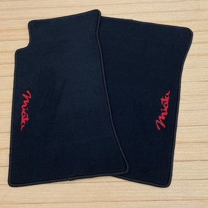 Peut inclure: Deux tapis de sol de voiture noirs avec des logos "Miata" brodés en rouge.