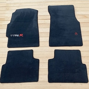 May include: Set of four black car floor mats with embroidered logos. The driver's side mat has "Integra Type R" in white with a red "R". The passenger side mat has a red "A" logo.
