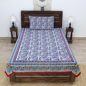 May include: A blue and white floral patterned bedsheet and pillowcase set. The bedsheet features a repeating pattern of birds and leaves in shades of blue, red, and yellow. The border is a contrasting design with floral and geometric elements. The set is displayed on a wooden bed frame.