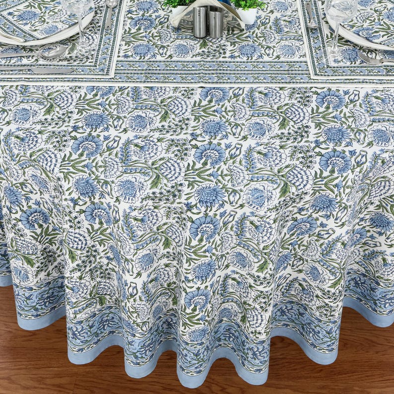 Round blue and white floral hand block printed cotton tablecloth, featuring intricate Indian design with green accents. Perfect dining table cover for farmhouse, cottagecore, or boho decor. Ideal for weddings, housewarming gifts, summer dining, or festive celebrations. Handmade by skilled artisans using traditional block printing techniques. Fits large round tables beautifully, adding elegance to your dining space.