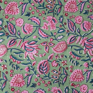 Beautiful hand block printed cotton tablecloth featuring floral patterns with pink and green accents. This vibrant Indian dining table cover adds a touch of bohemian charm to your kitchen or dining space. Ideal for everyday use, festive meals, or special occasions like housewarmings, weddings, baby showers, or dinner parties. Styled on a wooden table with white plates, cutlery, glasses, and a centerpiece flower vase.