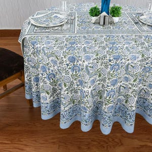 Round blue and white floral hand block printed cotton tablecloth, featuring intricate Indian design with green accents. Perfect dining table cover for farmhouse, cottagecore, or boho decor. Ideal for weddings, housewarming gifts, summer dining, or festive celebrations. Handmade by skilled artisans using traditional block printing techniques. Fits large round tables beautifully, adding elegance to your dining space.