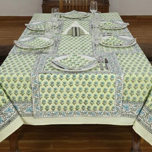 Könnte beinhalten: Ein Esstisch mit einer Tischdecke mit Blumenmuster, Tischsets und passenden Tellern. Die Tischdecke ist hellgrün mit blauen und braunen Blumenmustern. Der Tisch ist für eine Mahlzeit mit Gläsern, Servietten und Besteck gedeckt.