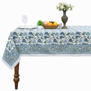 Puede incluir: Un mantel rectangular con base blanca y un patrón floral repetitivo en azul y verde. El diseño incluye bandas horizontales de flores y hojas estilizadas, rematado con un borde a rayas a lo largo de los extremos de la tela.