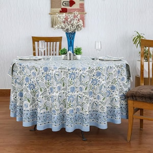 Round blue and white floral hand block printed cotton tablecloth, featuring intricate Indian design with green accents. Perfect dining table cover for farmhouse, cottagecore, or boho decor. Ideal for weddings, housewarming gifts, summer dining, or festive celebrations. Handmade by skilled artisans using traditional block printing techniques. Fits large round tables beautifully, adding elegance to your dining space.