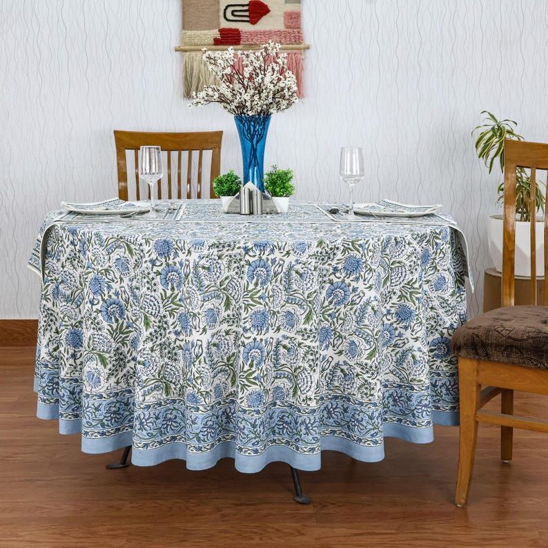 Round blue and white floral hand block printed cotton tablecloth, featuring intricate Indian design with green accents. Perfect dining table cover for farmhouse, cottagecore, or boho decor. Ideal for weddings, housewarming gifts, summer dining, or festive celebrations. Handmade by skilled artisans using traditional block printing techniques. Fits large round tables beautifully, adding elegance to your dining space.
