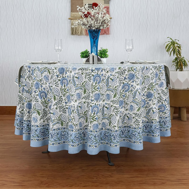 Round blue and white floral hand block printed cotton tablecloth, featuring intricate Indian design with green accents. Perfect dining table cover for farmhouse, cottagecore, or boho decor. Ideal for weddings, housewarming gifts, summer dining, or festive celebrations. Handmade by skilled artisans using traditional block printing techniques. Fits large round tables beautifully, adding elegance to your dining space.