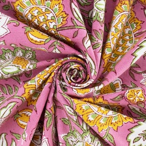May include: Close-up of a pink fabric with a floral pattern. The design features yellow and green flowers with white accents and green leaves. The fabric is gathered in a spiral, showcasing the detailed print.