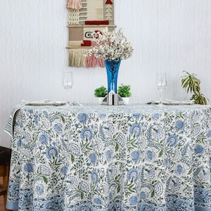 Round blue and white floral hand block printed cotton tablecloth, featuring intricate Indian design with green accents. Perfect dining table cover for farmhouse, cottagecore, or boho decor. Ideal for weddings, housewarming gifts, summer dining, or festive celebrations. Handmade by skilled artisans using traditional block printing techniques. Fits large round tables beautifully, adding elegance to your dining space.