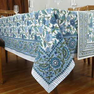May include: A rectangular tablecloth featuring a white base with a repeating blue and green floral pattern. The design includes a wide border with stylised flowers and leaves, finished with a striped edge detail along the bottom hem of the fabric.