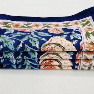 Puede incluir: Un conjunto de cinco servilletas de algodón azul con un estampado floral en tonos naranja, blanco y verde. Las servilletas tienen un borde azul oscuro.