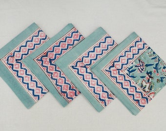 Op de afbeelding: Set van vier blauwe katoenen servetten met een geometrische rand in roze en blauw. De servetten hebben aan één kant een bloemenpatroon.