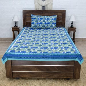 Op de afbeelding: Een blauw en wit bloemenpatroon beddengoed en kussensloop set. Het beddengoed heeft een herhalend patroon van blauwe bloemen met groene bladeren op een witte achtergrond. De rand is donkerblauw met een decoratief ontwerp.
