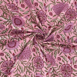 Beautiful hand block printed cotton tablecloth featuring floral patterns with pink and red accents. This vibrant Indian dining table cover adds a touch of bohemian charm to your kitchen or dining space. Ideal for everyday use, festive meals, or special occasions like housewarmings, weddings, baby showers, or dinner parties. Styled on a wooden table with white plates, cutlery, glasses, and a centerpiece flower vase.