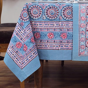 Puede incluir: Un mantel de mesa de algodón azul con un patrón floral rosa y blanco. El mantel tiene un borde con un diseño geométrico.