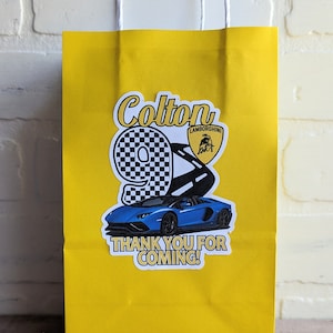 May include: Yellow paper gift bag with a sticker featuring a blue Lamborghini with a checkered number 9, the text "Colton" and "Lamborghini" and the words "Thank you for coming!"