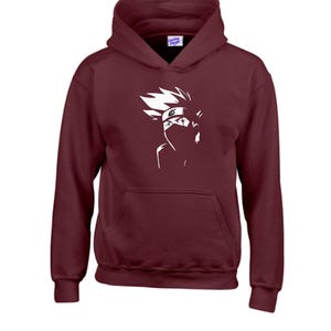 May include: A maroon hoodie with a white graphic of a character's face, featuring spiky hair and a mask. The hoodie has a front pocket and a hood. The brand name "Clothing Studio" is visible on the tag.