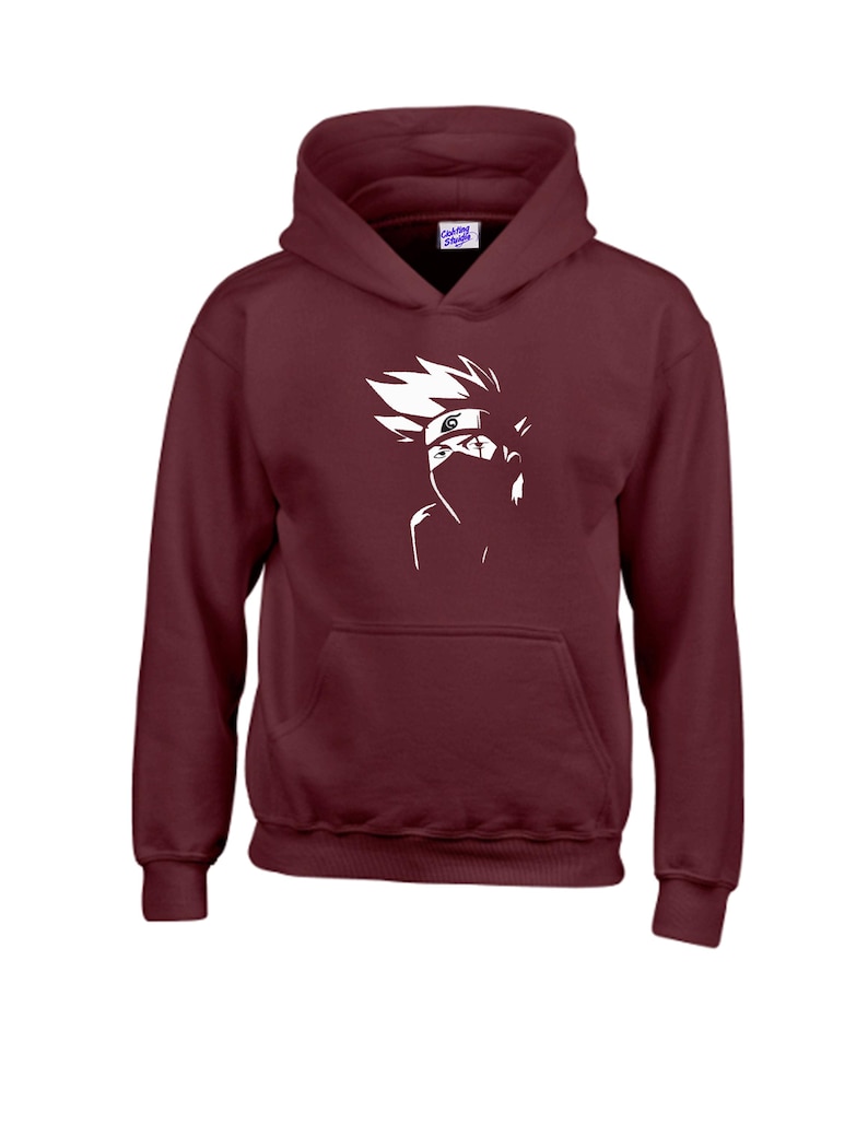 May include: A maroon hoodie with a white graphic of a character's face, featuring spiky hair and a mask. The hoodie has a front pocket and a hood. The brand name "Clothing Studio" is visible on the tag.