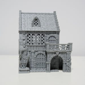 May include: A grey miniature castle with a detailed stone facade. The model features arched doorways, a statue, and a balcony with decorative railings. The roof is textured to resemble shingles.