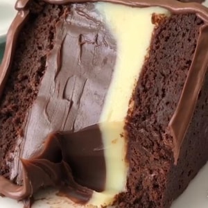 Pode incluir: Um bolo de chocolate com recheio branco e marrom, coberto com cobertura de chocolate. O bolo foi cortado e uma mordida foi dada.