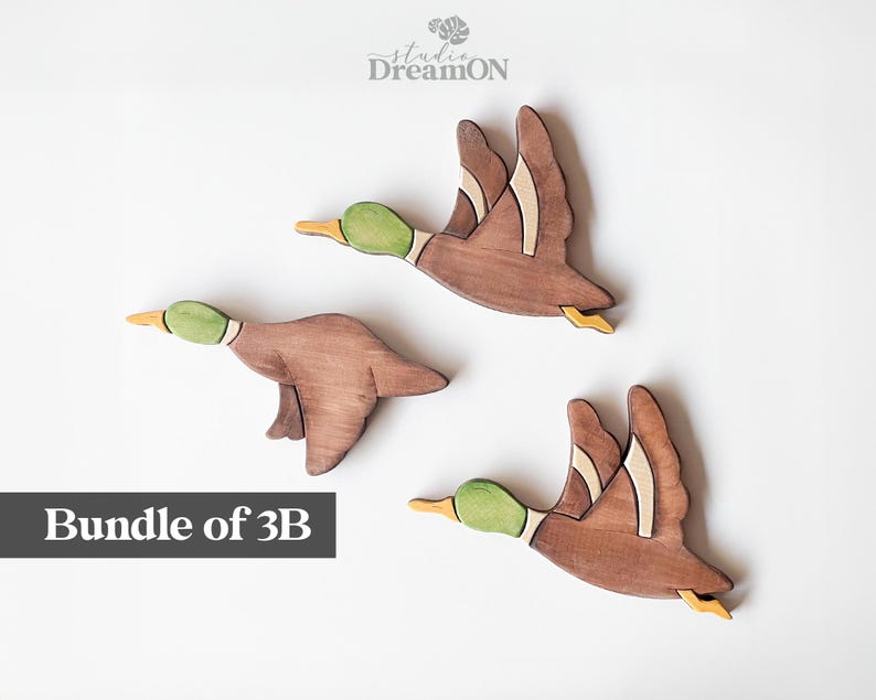K&ouml;nnte beinhalten: Paket mit 3B Holz-Enten-Wanddekoration. Die Enten sind braun bemalt mit gr&uuml;nen K&ouml;pfen und gelben Akzenten. Sie fliegen in verschiedene Richtungen.