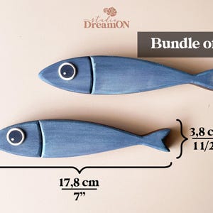 May include: Two blue wooden fish decorations, each 7 inches long, with white and black eye details. The fish are part of a bundle of two, perfect for nautical or coastal decor.