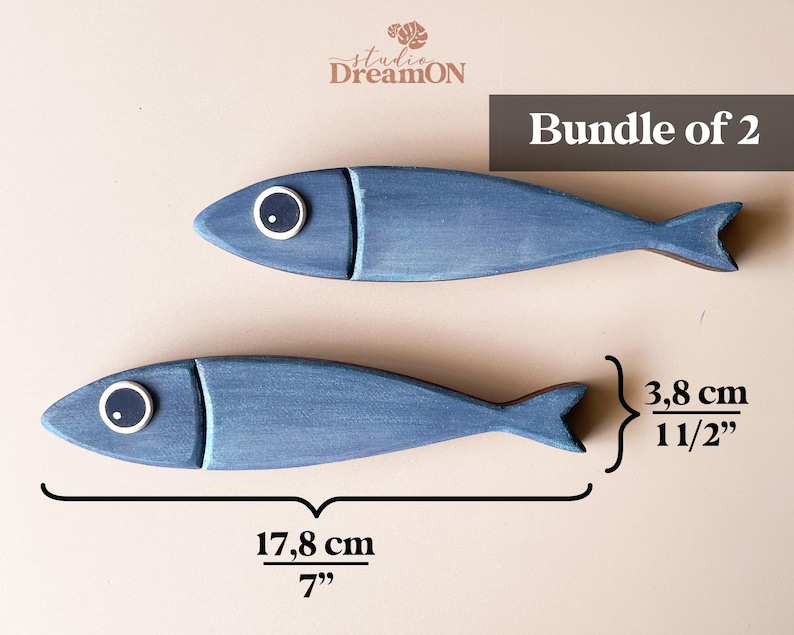May include: Two blue wooden fish decorations, each 7 inches long, with white and black eye details. The fish are part of a bundle of two, perfect for nautical or coastal decor.