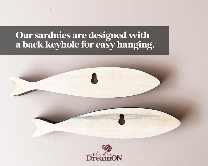 May include: Two wooden fish-shaped wall decorations. The fish are light-colored with a keyhole on the back for hanging. The text on the image says, "Our sardnies are designed with a back keyhole for easy hanging."