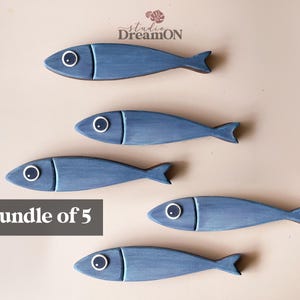 May include: Five blue wooden fish decorations with white and black eye details. The fish have a simple, stylized design and are arranged on a neutral background. The text "Bundle of 5" is displayed in a gray rectangle.