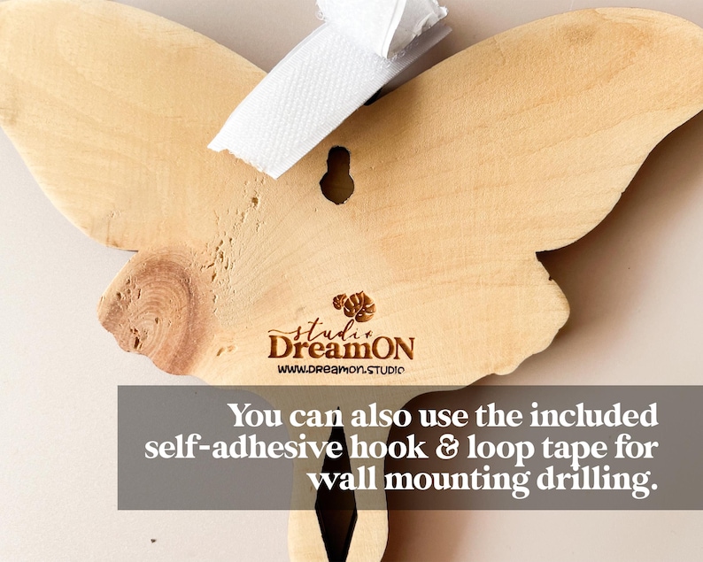 K&ouml;nnte beinhalten: Eine h&ouml;lzerne Schmetterlings-Wanddekoration mit nat&uuml;rlicher Holzoptik. Der Schmetterling hat oben ein Loch zum Aufh&auml;ngen und der Text "studi DreamON www.dreamon.STUDIO" ist unten eingraviert. Sie k&ouml;nnen auch das mitgelieferte selbstklebende Haken- und Schleifenband f&uuml;r die Wandmontage verwenden.