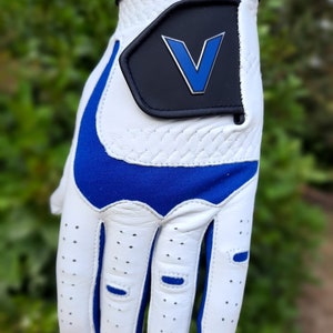 Op de afbeelding: Witte golfhandschoen met een blauwe accent en een zwarte patch met een blauw "V" logo.