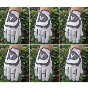 Puede incluir: Seis guantes de golf blancos con detalles negros y un logotipo "V" blanco en el dorso de la mano.
