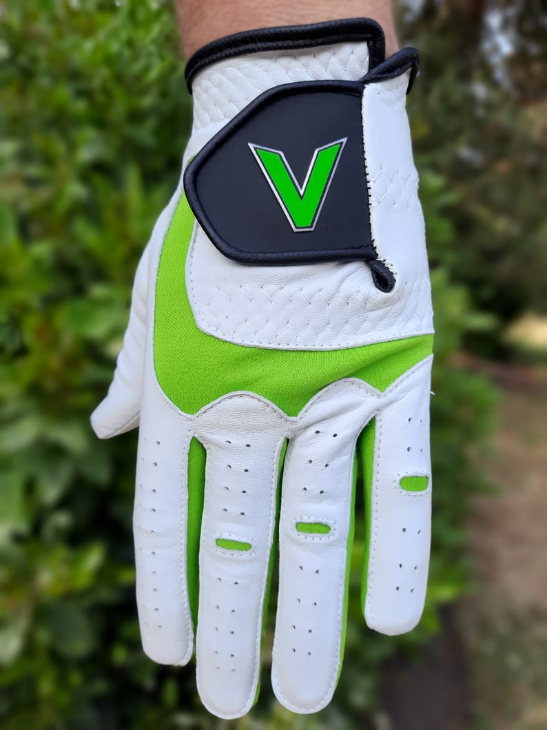 Op de afbeelding: Witte golfhandschoen met groene accenten en een zwarte patch met een groene "V" op de rug van de hand.