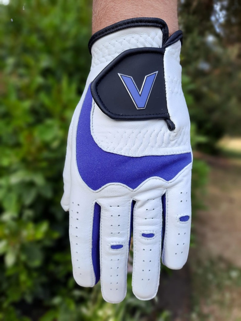 Op de afbeelding: Witte golfhandschoen met een paarse palm en een zwarte patch met een blauwe "V" op de achterkant van de hand.