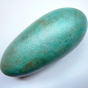 May include: An oval-shaped object with a textured surface. The object is teal with brown and bronze patches, giving a weathered look. The shape is smooth and symmetrical. The object is approximately 15 cm in length.