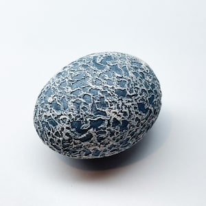 May include: A textured, oval-shaped decorative object. The object has a dark blue base color with a silver-colored, web-like pattern across its surface. The object is set against a white background.