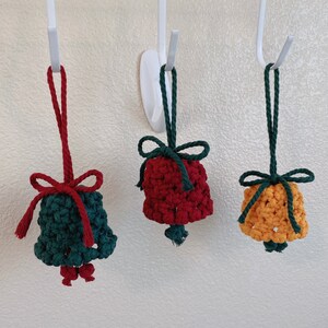 May include: Three crocheted bell ornaments hanging from hooks. The bells are red, green, and yellow.