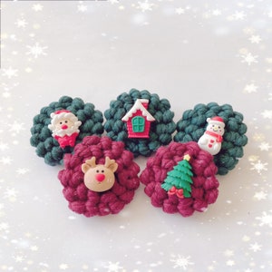 May include: Five Christmas-themed felt ornaments with different designs. The ornaments are green and red and feature a snowman, a house, a reindeer, a Santa Claus, and a Christmas tree.