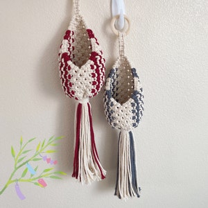 May include: Two macrame plant hangers, one red and white and one gray and white, hanging from a white wall.