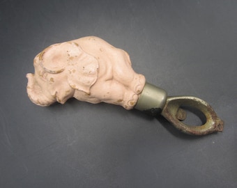Op de afbeelding: Een roze keramische olifant flessenopener met een metalen opener aan het uiteinde. De olifant ligt op zijn zij met zijn slurf omhoog.