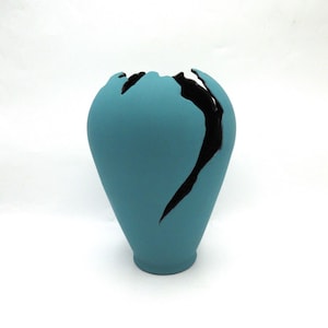 May include: A teal blue ceramic vase with a crack down the side. The crack is filled with black paint.
