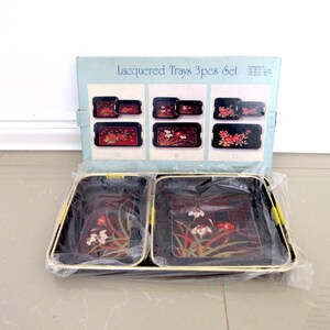 May include: A set of three black lacquered trays with gold trim and floral designs. The trays are packaged in a box with the text "Lacquered Trays 3 pcs Set".