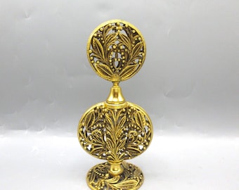 May include: Ornate gold-colored perfume bottle with a decorative floral design. The bottle has a round base, an oval midsection, and a circular top, all featuring intricate leaf and vine patterns. The metal has a polished finish.