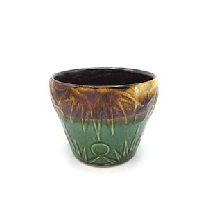 May include: A small, green and brown ceramic planter with a decorative design. The planter has a rounded bottom and a wide, open top.