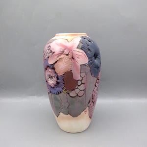 May include: A ceramic vase with a floral design. The vase is decorated with pink, purple, and brown flowers and leaves. The vase is approximately 10 inches tall.