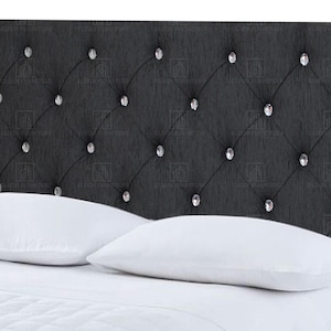 May include: A dark grey upholstered headboard with a diamond-tufted design. The headboard features crystal-like button accents. Two white pillows rest on a white bed. The headboard is a stylish addition to any bedroom.
