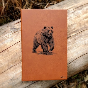 May include: Brown leather journal with an engraved image of a bear and the name "Alex" on the front.