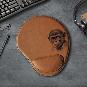 May include: Brown leather mouse pad with a black and white image of a monkey's face.