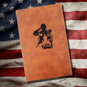 May include: A brown leather journal with a silhouette of a soldier saluting with an American flag in the background. The journal has the name "Mike" embossed on the bottom right corner.