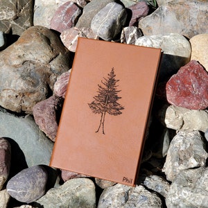 May include: A brown leather journal with a tree design and the name "Phil" embossed on the cover.